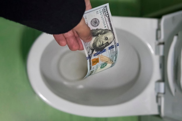 Concept of senseless waste of money loss useless waste large water costs Flushing one hundred dollars down the toilet loss of money losing money