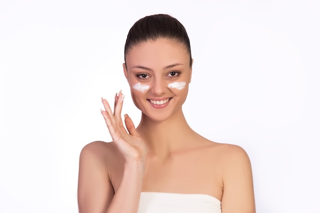 Concept of skin care, keeping healthy skin, moisturizing, different skin products. Young women with creme under her eyes.