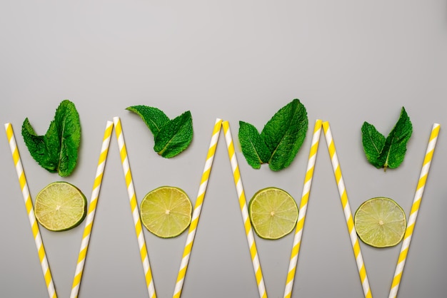 Concept of summer refreshing drinks in minimalism style from cocktail tubes and lime with mint on gray background