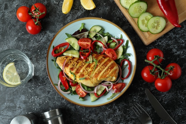 Concept of tasty eating with salad with grilled chicken on black textured table