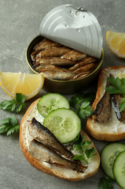 Concept of tasty snack with sandwiches with sprats on gray textured background