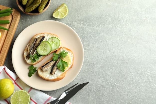 Concept of tasty snack with sandwiches with sprats on gray textured background