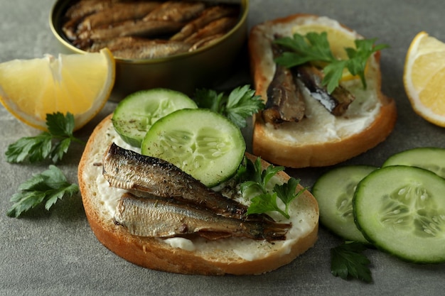 Concept of tasty snack with sandwiches with sprats on gray textured background