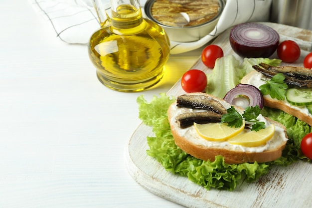 Concept of tasty snack with sandwiches with sprats on white wooden background