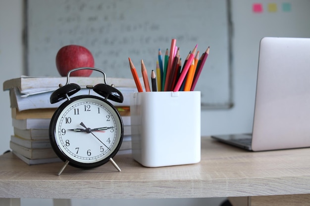 Concept to teacher's day Pens apple pencils books alarm clock and laptop on the table