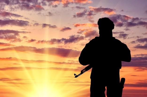 Concept of terrorism. Silhouette of a terrorist with a weapon against a background of a sunset