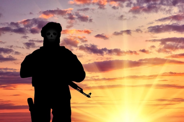 Concept of terrorism. Silhouette of a terrorist with weapons and a skull face at sunset