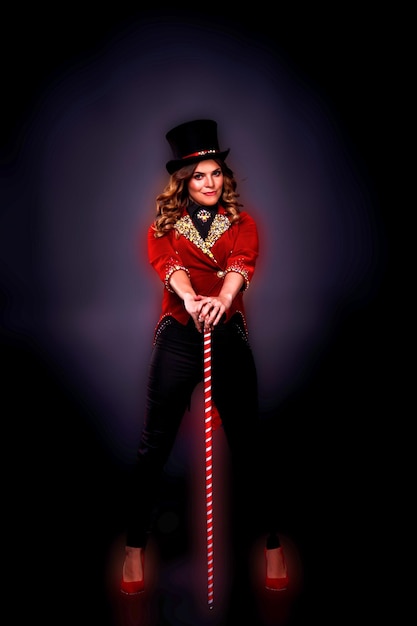 Concept of theatre performance Woman magician illusionist circus with cane and top hat in theatrical clothes shows and smiles at black background