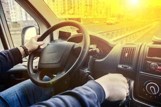 concept of a truck driver, driver's hands on the steering wheel on a sunny day in summer.