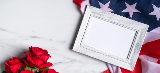 Concept of U.S. Independence day or Memorial day. National flag and red rose over bright marble table background with picture frame.