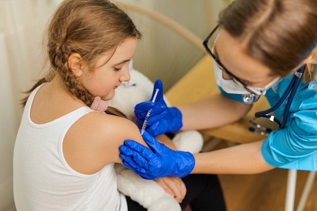 The concept of vaccination. Female doctor vaccinating cute little girl in clinic