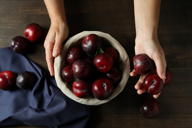 Concept with plums and hands on wooden table.