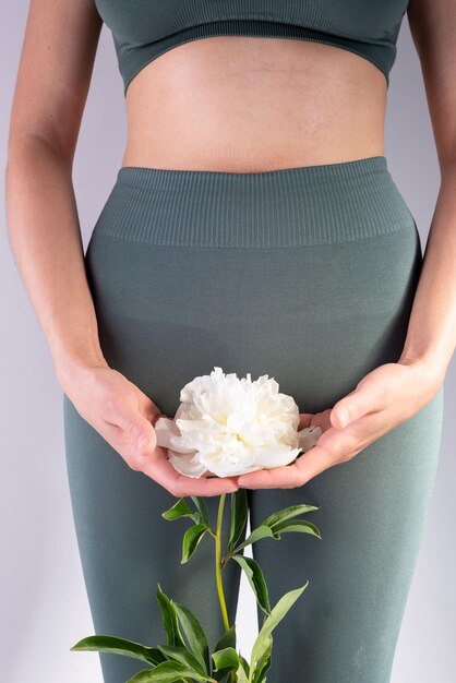 Concept of women's health a girl in leggings holding a white flower in her hands on a gray background