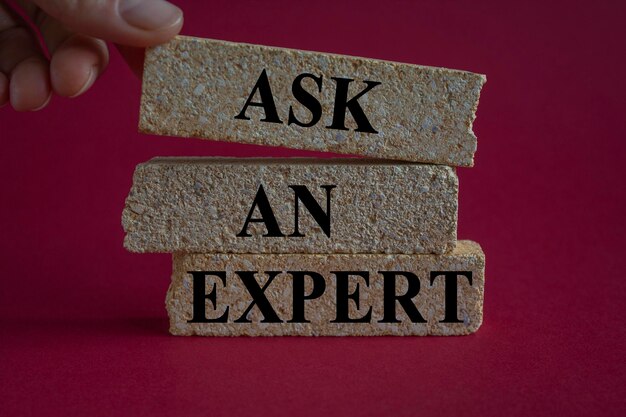 Concept words Ask an expert on brick blocks on a beautiful red background Businessman hand