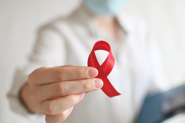 Concept World AIDS and hiv day A female doctor in a white coat holds red ribbon on white background