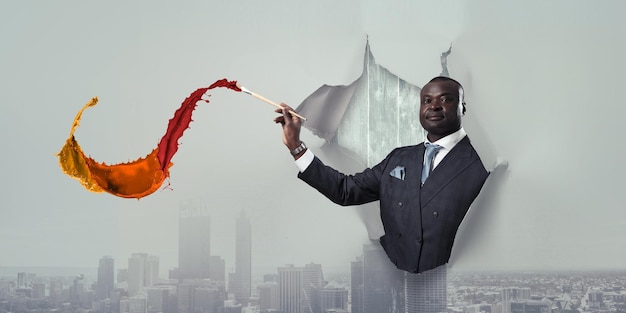 Conceptual image of ambitious and creative businessman in black suit holding paintbrush in hand