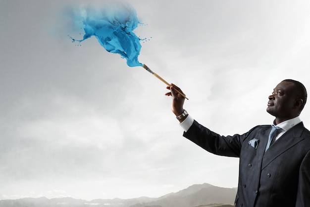 Conceptual image of ambitious and creative businessman in black suit holding paintbrush in hand