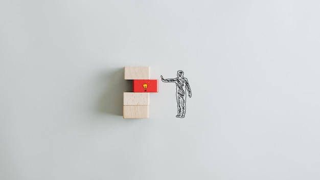 Conceptual image of business idea and vision with silhouette of a man pushing a red wooden peg with lightbulb in to a stack of pegs Over grey background