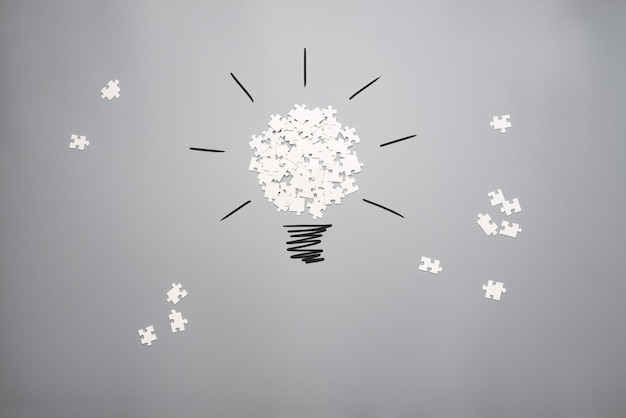 Conceptual image of vision and idea with a pile of white scattered puzzle pieces forming a light bulb on a grey background.