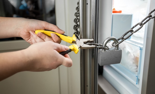 Conceptual photo of woman trying to cut chain on fridge with pliers