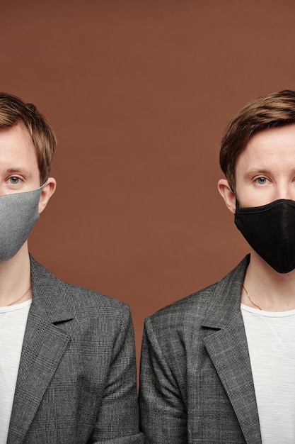 Conceptual photo of young twins in facial masks standing against brown background