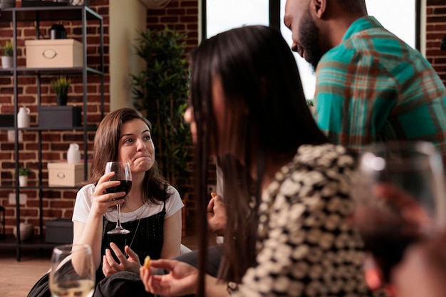 Concerned caucasian woman listening, hearing attentively african american friend, partner, colleague, associate questions at coworkers meeting, drinking wine, eating snacks, bread sticks.