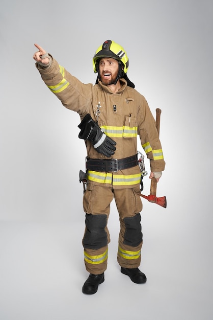 Concerned firefighter in uniform shouting while pointing away indoors front view of excited bearded