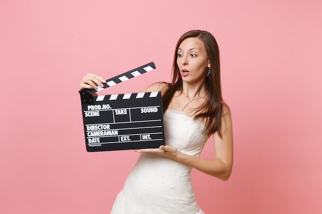 Concerned shocked woman in white dress holding classic black film making clapperboard