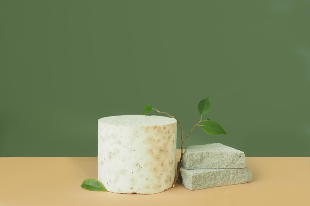 Concrete cylindrical pedestal, ficus branch and concrete plates on a beige green background.