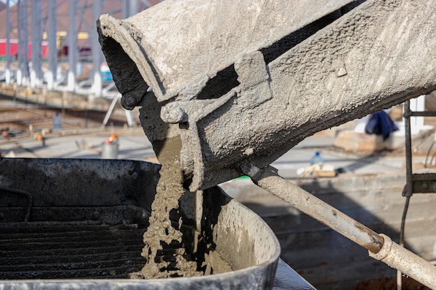 A concrete mixer truck pours concrete into a pump at a construction site.