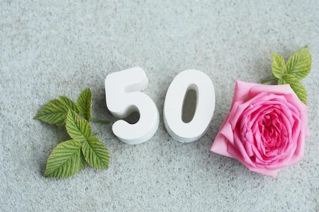 Concrete number 50 and a beautiful rose with petals and hearts on a concrete gray background.