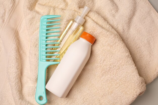 Conditioner, comb and revitalizing hair oil lying on a crumpled towel in a bathroom. Copy space