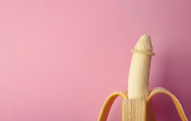 Photo condom and banana on pink background with copy space