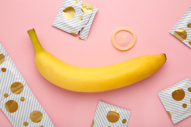 Condom and banana on pink background with copy space