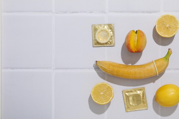 Condom on banana with peach and lemon on light background place for text