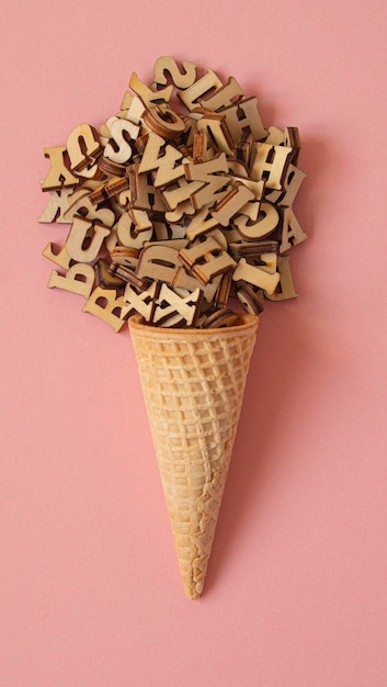 Cone ice cream formed with a ball of wooden letters on a pink background