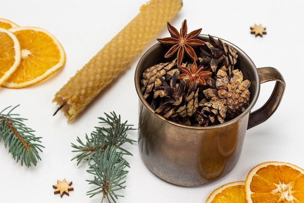 Cones in a metal mug a candle sprigs of spruce and dry orange slices