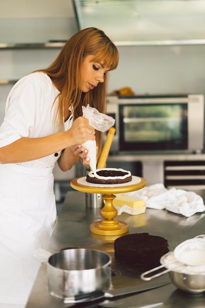 Confectioner girl is preparing a cake biscuit with white cream and chocolate cooking cakes