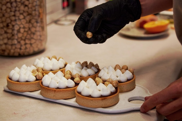 Confectioner is decorating a tarts with nuts in a cafe French aesthetic hazelnut creamy tarts in the row