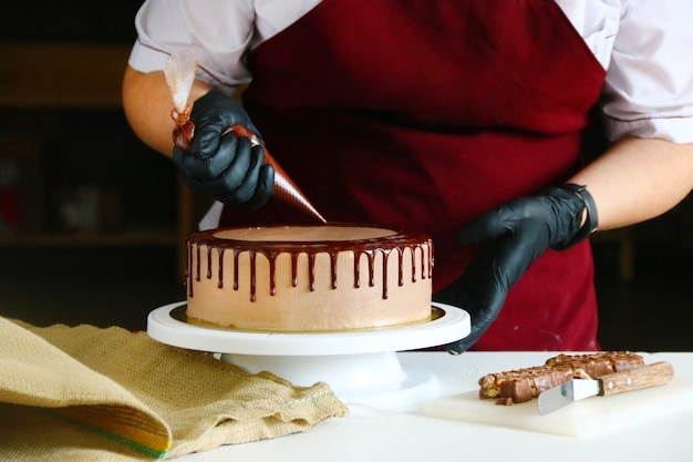 Confectioner squeezes liquid chocolate from a pastry bag on to a cream biscuit cake