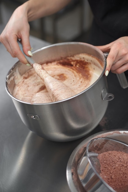 Confectioner wearing black uniform stirs cream work in pastry shop the workflow of  the kitchen