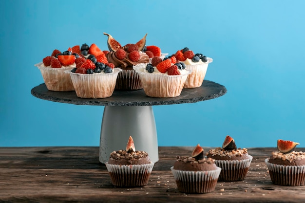 Confectionery on stand. Vanilla and chocolate muffins with fresh berries on blue background. Side view, copy space.