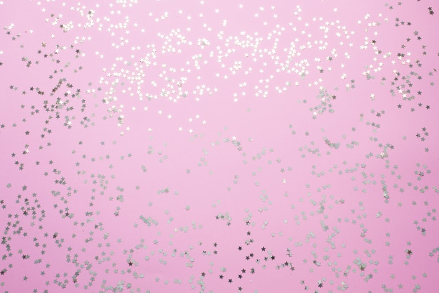 Confetti of gold stars glisten on a pink background. Festive holiday pastel backdrop.