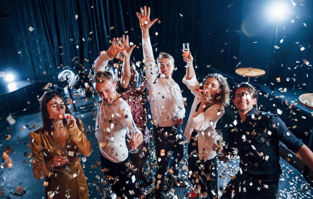 Confetti is in the air Group of cheerful friends celebrating new year indoors with drinks in hands