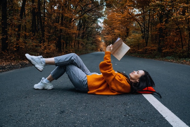 Confidence woman with book sitting on the road with autumn tree around new life path choice ambition