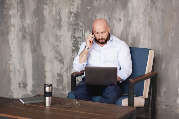 Confident adult man talks on the phone sitting at the computer