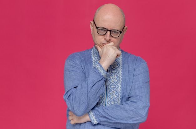 Confident adult slavic man in blue shirt wearing optical glasses holding his chin and 