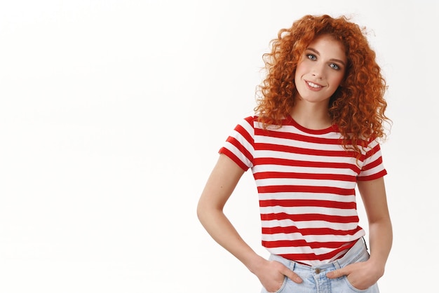 Confident assertive gorgeous curlyhaired redhead woman hold hands pockets selfassured smiling tilting head wearing striped summer tshirt enthusiastic coworker determined make project good