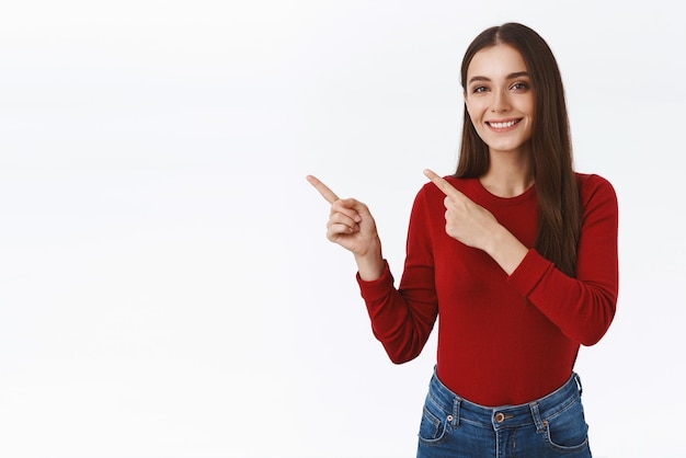 Confident assertive pretty modern brunette girl in red sweater promoting offer advice link or recommend shop product pointing upper left corner smiling with satisfied selfassured expression