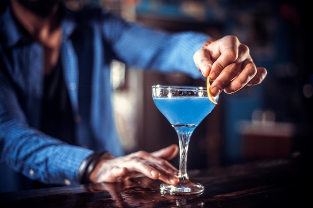 Confident bartender places the finishing touches on a drink while standing near the bar counter in pub